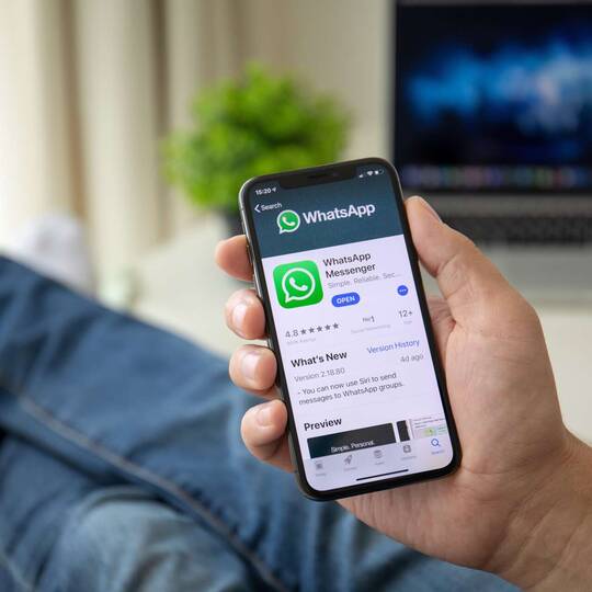 Person mit hochgelegten Beinen hält Smartphone mit WhatsApp Anzeige auf Bildschirm