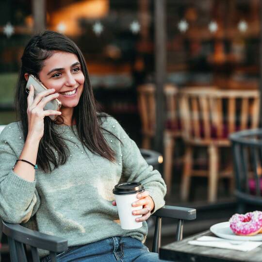 Frau sitzt in Café mit Smartphone am Ohr