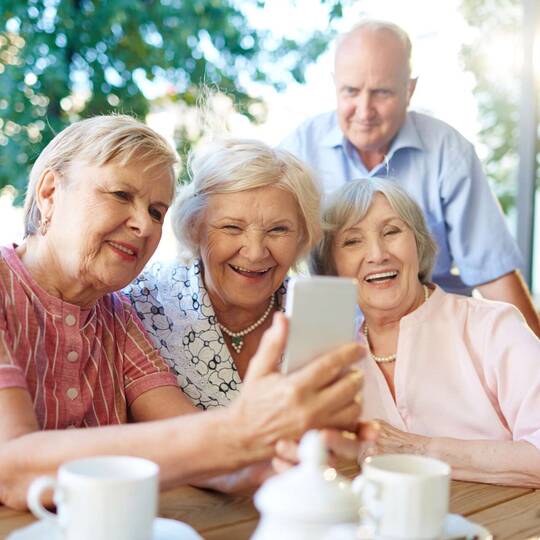 Mehrere ältere Personen schauen gemeinsam fröhlich auf ein Smartphone Display