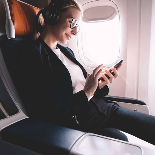 Frau sitzt auf Flugzeugsitz und bedient Smartphone