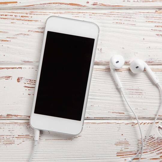 weißes iPhone liegt mit Kopfhörern auf Holz