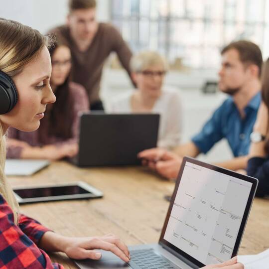 Frau mit Over Ear Kopfhörern sitzt vor Personengruppe