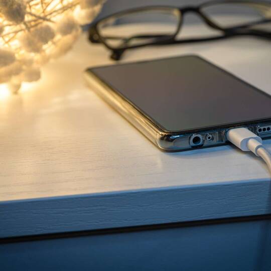 Smartphone liegt auf Nachttisch mit Ladekabel