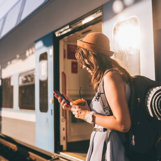 Frau steht vor Zug und guckt auf ihr Smartphone