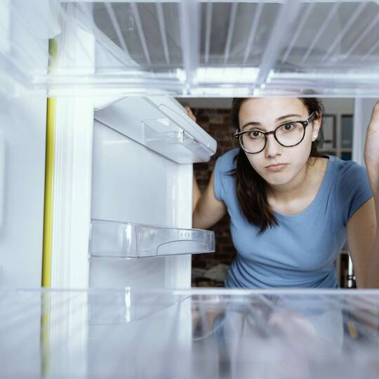 Eine Frau guckt in einen leeren Kühlschrank