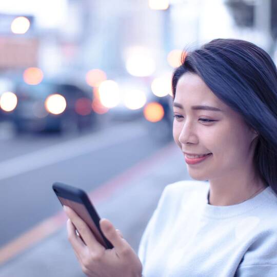 eine Frau steht an der Straße und schaut auf ihr Smartphone