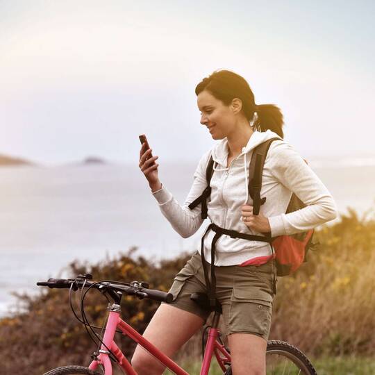 Sportlich gekleidete Frau auf Fahrrad in der Natur schaut auf Smartphone