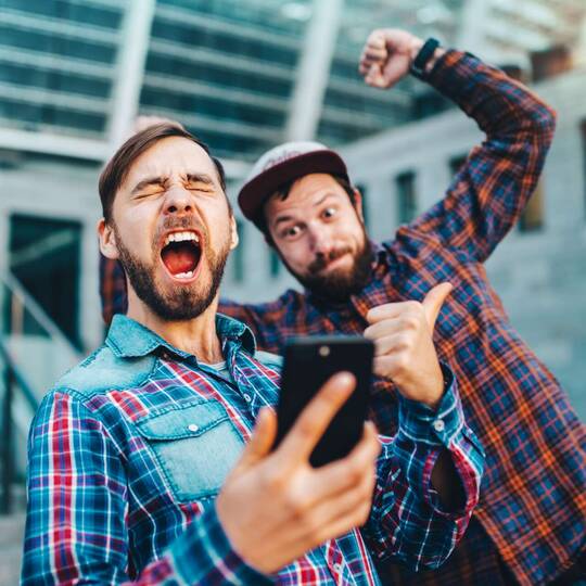 Zwei Männer schauen jubelnd auf Smartphone Display