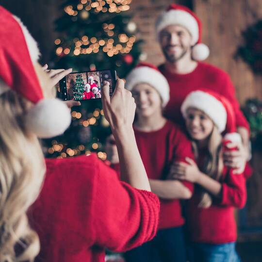 Frau macht Foto von ihrer Familie  vorm Weihnachtsbaum mit ihrem Smartphone