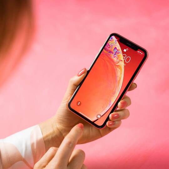 Person tippt auf iPhone mit rotem Hintergrundbild