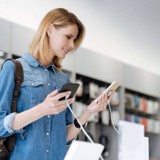 Frau im Elektronikladen mit zwei verschiedenen Smartphones in den Händen