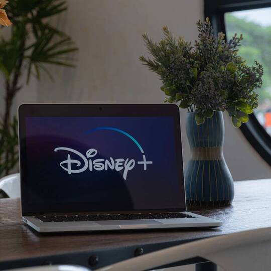 Laptop mit Disney+ Symbol auf Display auf Ablagefläche