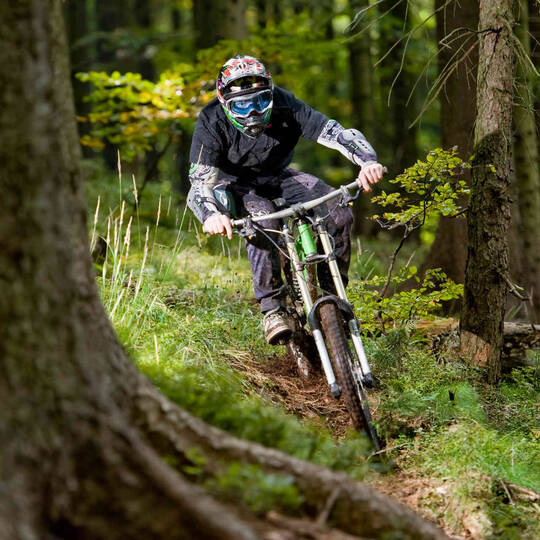 Mann mit Schutzausrüstung fährt bergab durch Wald auf Mountainbike.