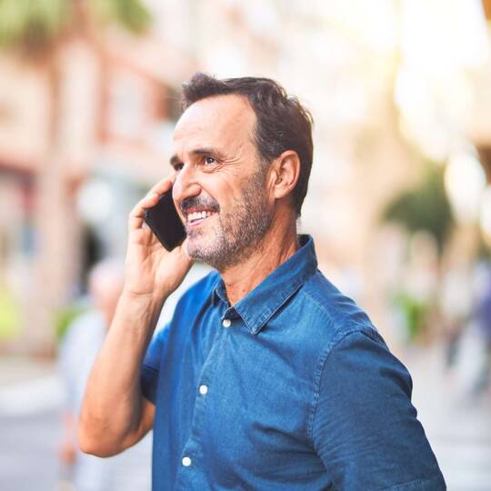 Mann im Jeanshemd telefoniert fröhlich auf Straße