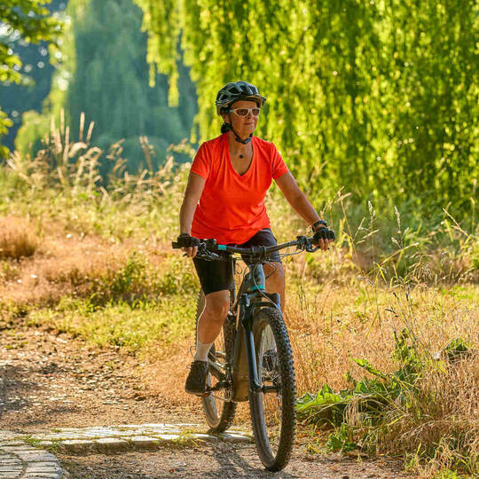 Frau fährt auf E-Crossbike über Natur-Radweg.