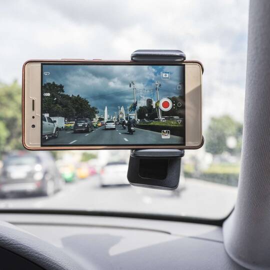 Smartphone mit eingeschalteter Videofunktion in einer Halterung an der Windschutzscheibe eines Autos