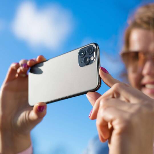 Frau hält lächelnd iPhone 11 Pro hoch, um ein Foto zu schießen