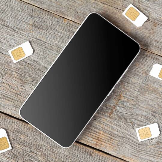 Smartphone liegt auf Holzboden umgeben von SIM-Karten