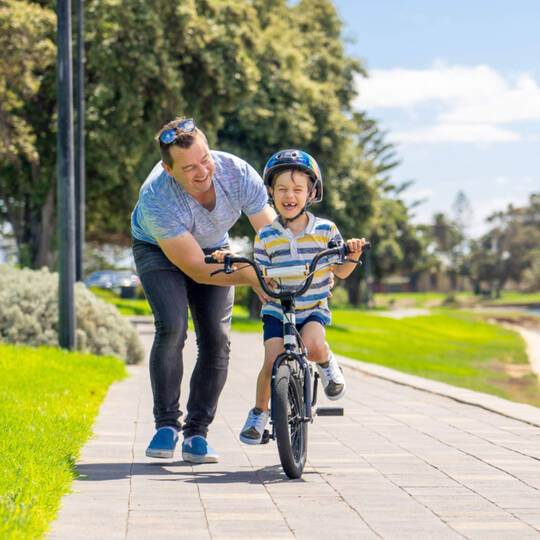 Ein Vater bringt seinem lachendem Kind Rad fahren bei