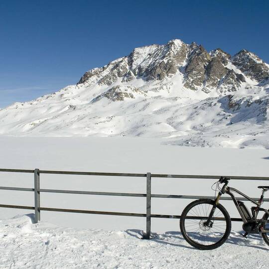 Fahrrad lehnt an inem Zaun vor wuinterlicher Bergkulisse