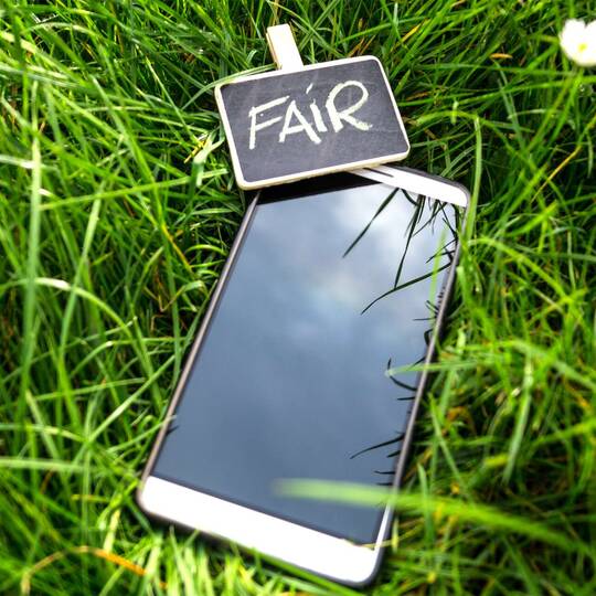 Smartphone liegt im Gras mit einer kleinen Tafel dabei, auf welcher "FAIR" steht
