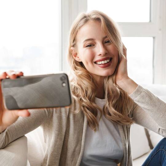 Frau hält Smartphone vor ihrem Gesicht und lächelt