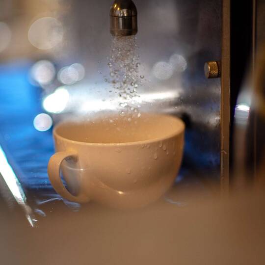Wsser beim Kaffeemaschinenreinigungsprozes fließt in Tasse