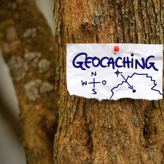Ein Zettel mit dem Wort Geocaching hängt an einem Baum