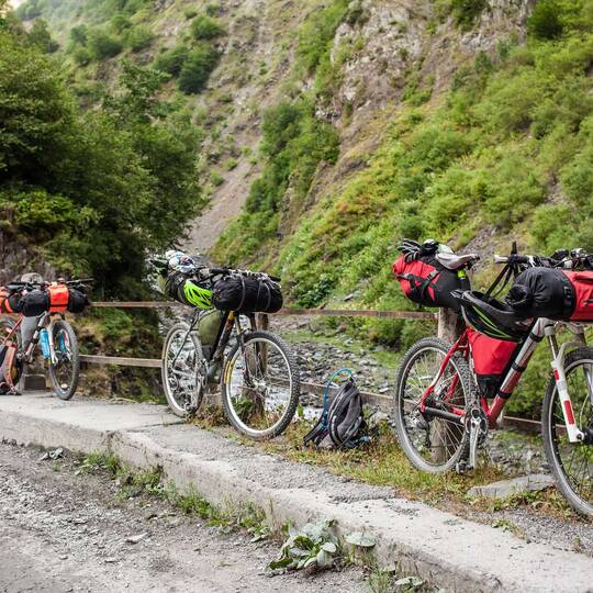Drei Fahrräder in bergigem Gelände, die mit rot-schwarzen Bikepacking-Taschen versehen sind