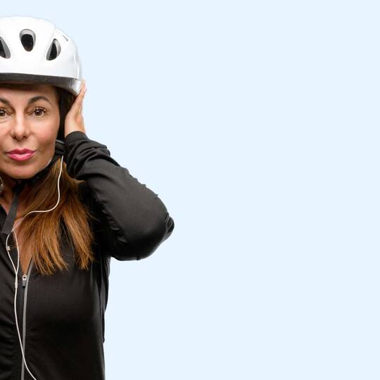 Frau mit aufgesetztem Fahrradhelm hält sich die Ohren zu