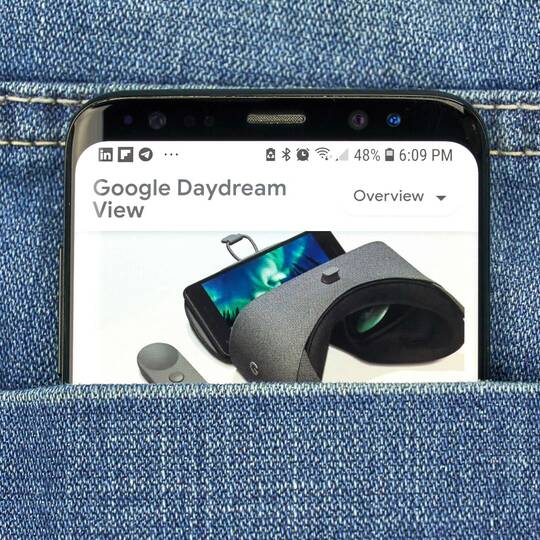 Schwarzes Smartphone in einer Hosentasche. Auf dem Bildschirm wird ein Bild der Google Daydream Brille gezeigt. 
