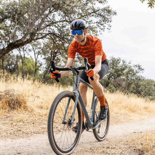 Mann mit Helm fährt auf Gravelbike über einen Weg durch die Natur.