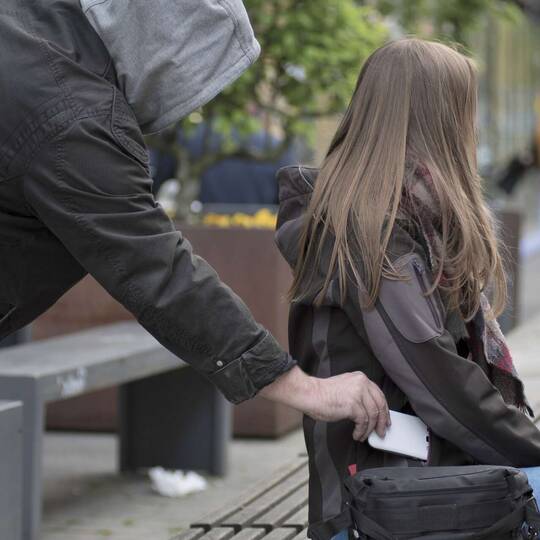 Mann mit Kapuze klaut unbemerkt Smartphone aus der Jackentasche einer Frau