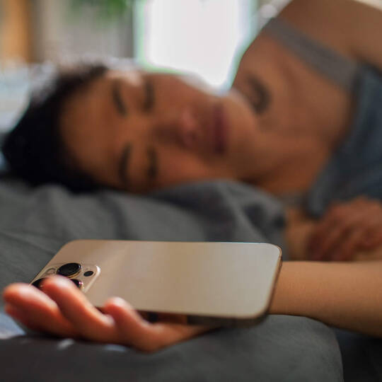 Frau schläft mit Smartphone in der Hand ein