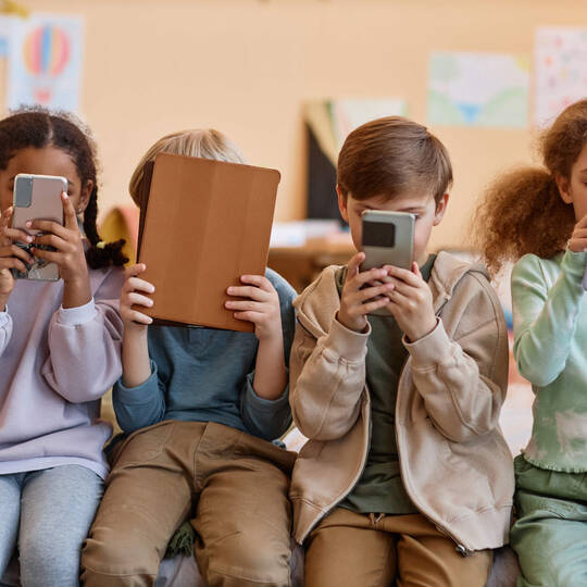 Kinder sitzen vor Smartphones und Tablets