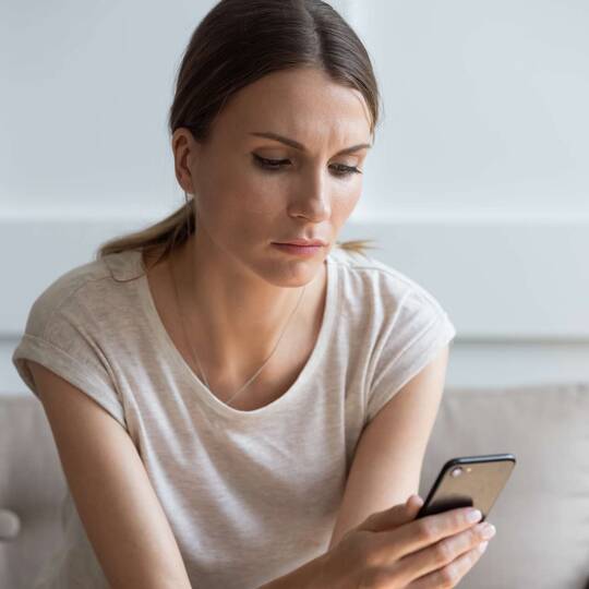 Frau sitzt auf einem Sofa mit Handy in der Hand