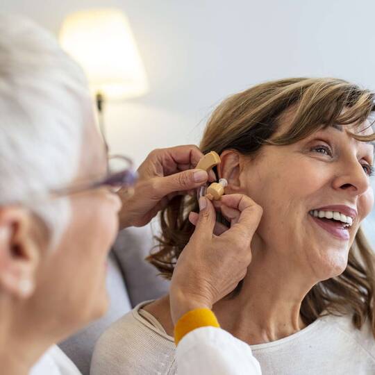 Frau nimmt am Ohr einer anderen Frau Anpassungen am Hörgerät vor