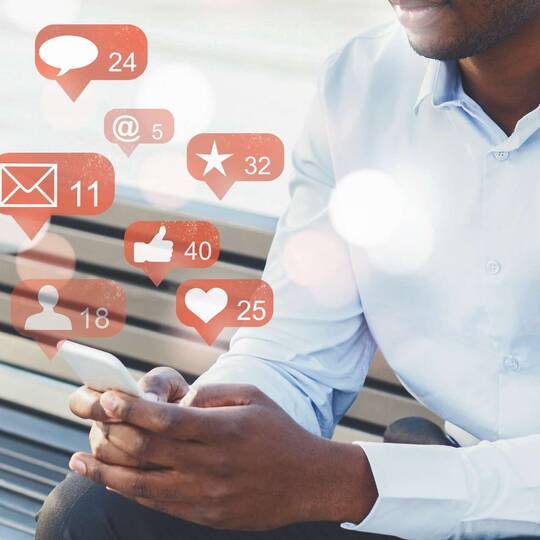 Mann hält Handy aus denen Social Media Symbole herauskommen