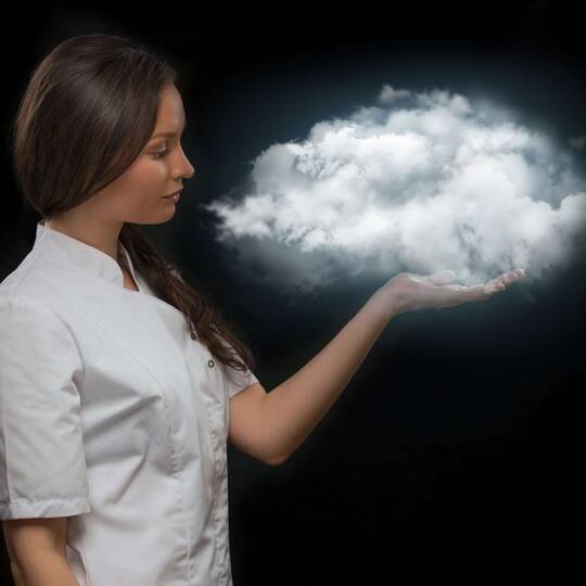 Frau im weißen, kurzärmligen Hemd vor dunklem Hintergrund hält Wolke schwebend über der Hand