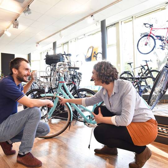 Zwei Personen, ein Kunde und der Verkäufer, befinden sich in einem Fahrradgeschäft. Der Kunde lässt sich vom Fachhändler beraten. 
