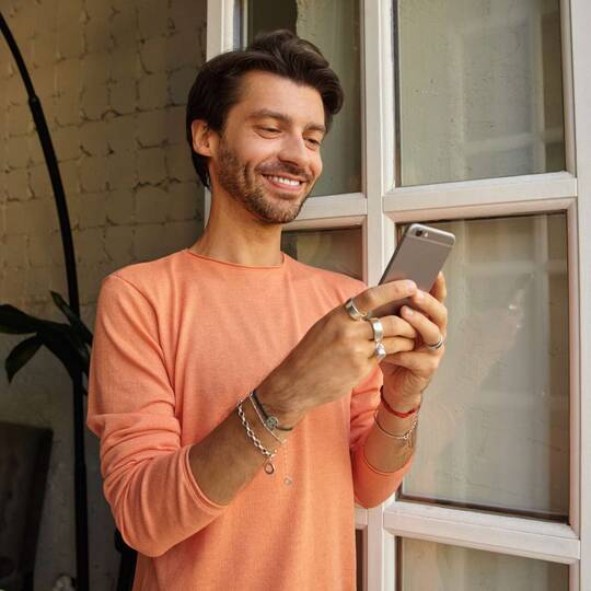 ein Mann steht am Fenster und lächelt in sein Smartphone