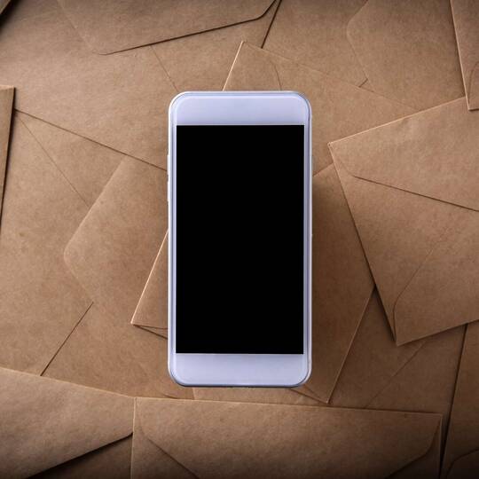 Smartphone liegt auf braunen Briefumschlägen