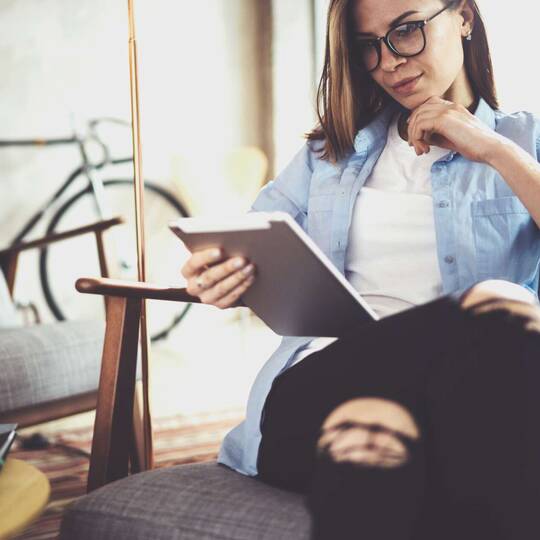 Frau in modernem Umfeld mit Jeanshemd hält iPad in der Hand