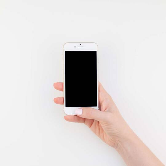 Hand hält Handy vor weißem Hintergrund