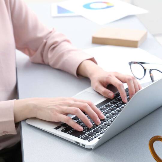 Person sitzt am Laptop und hat die Hände auf der Tastatur