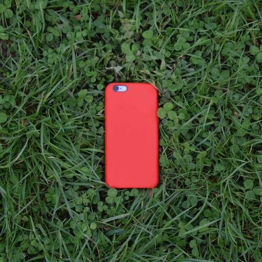 iPhone mit roter Hülle liegt im Gras