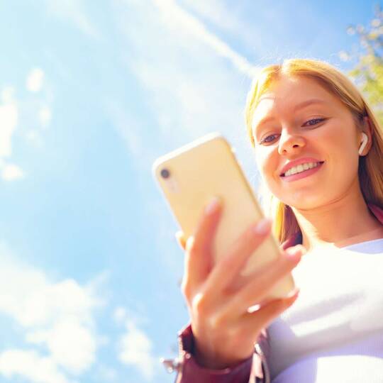 Junge Frau im Freien schaut lächelnd auf ihr Smartphone