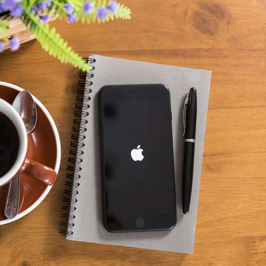 Bootendes iPhone liegt auf Notizbuch neben einer Tasse Kaffee