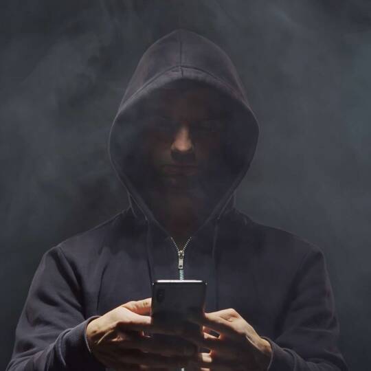 Mann im schwarzen Hoodie mit Smartphone in den Händen vor nebligem Umfeld