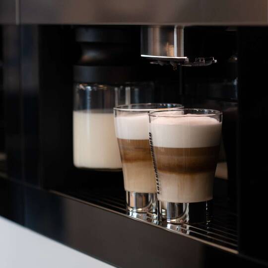 Zwei Gläser gefüllt mit Kaffeespezialität stehen unter Automat